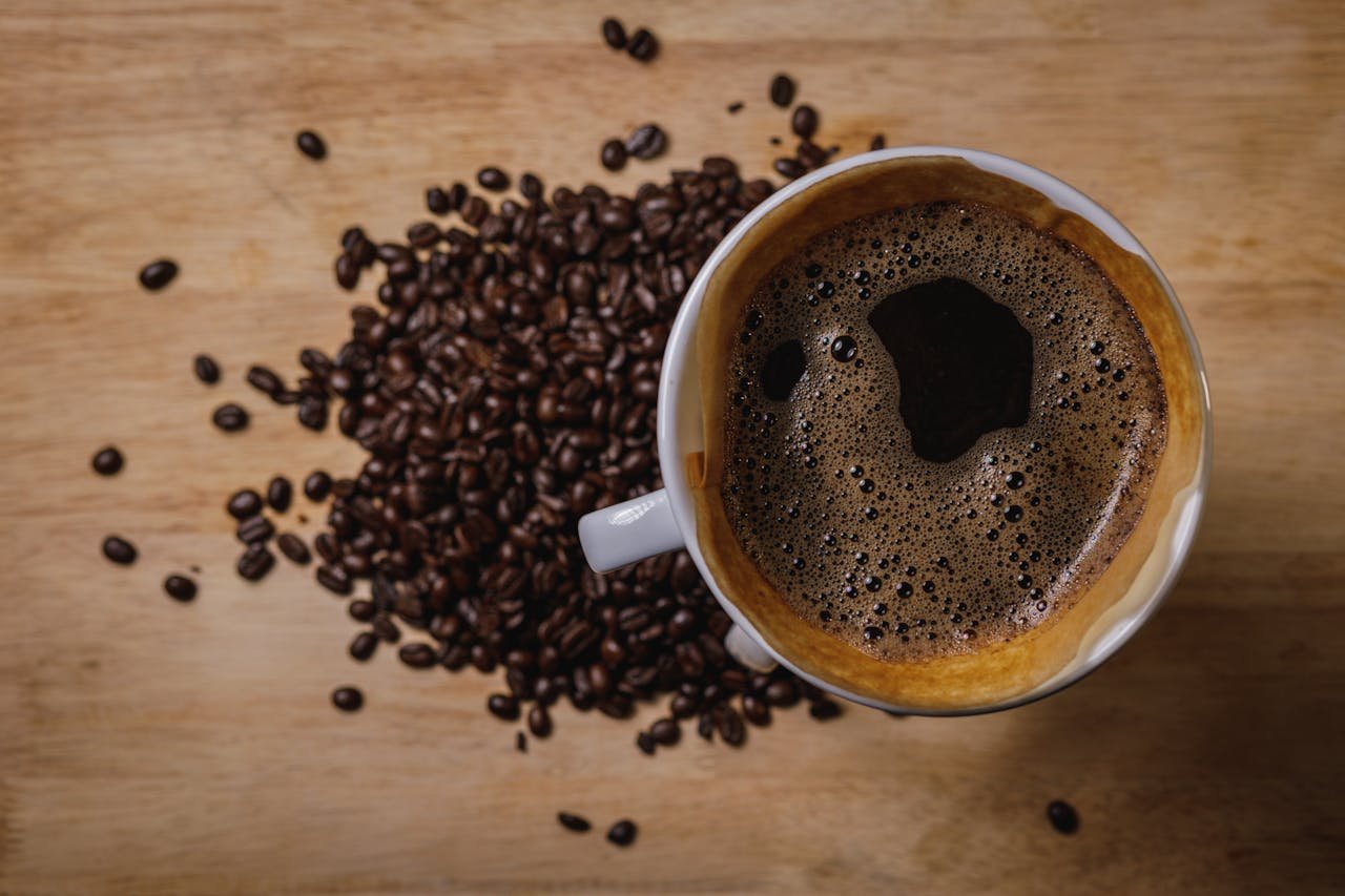 services-03 Close-up of a steaming cup of black coffee with scattered coffee beans on wooden background.