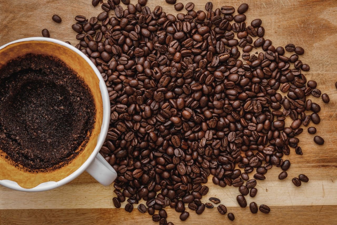 our-story Close-up of fresh coffee beans scattered next to a brewed cup on a wooden surface.