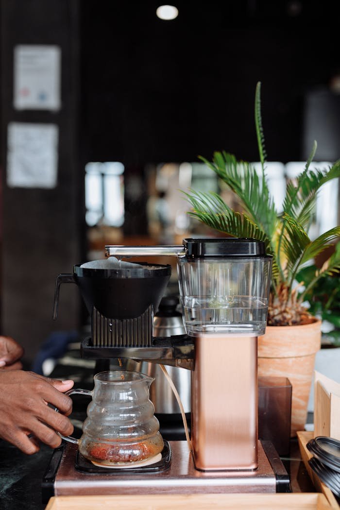 services-02 A stylish drip coffeemaker brewing fresh coffee indoors with a hand visible.